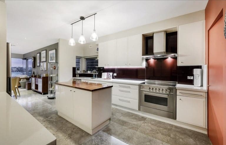 White Sydney kitchen with a timber-topped island and burgundy tiled splashback